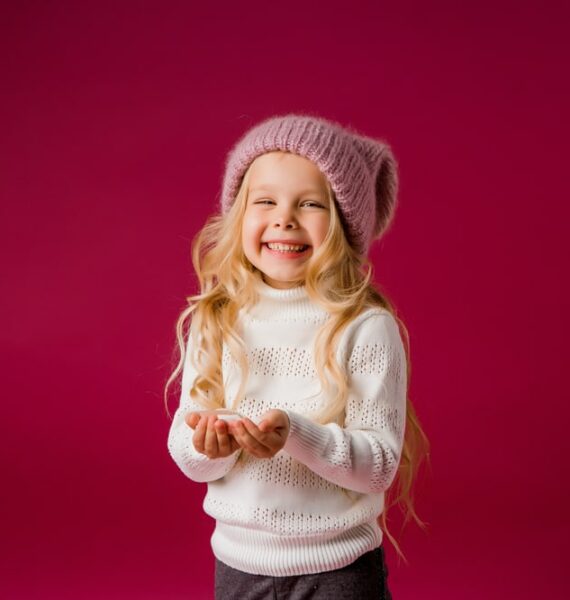 Une petite fille en pull rose sur fond rose.
