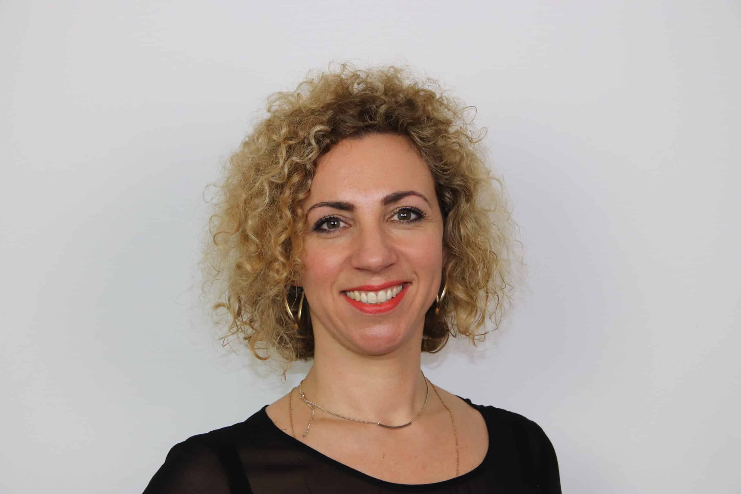Une femme aux cheveux bouclés souriante devant un mur Dore.