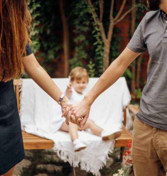 Une famille assise sur un banc dans un jardin, se tenant la main.
