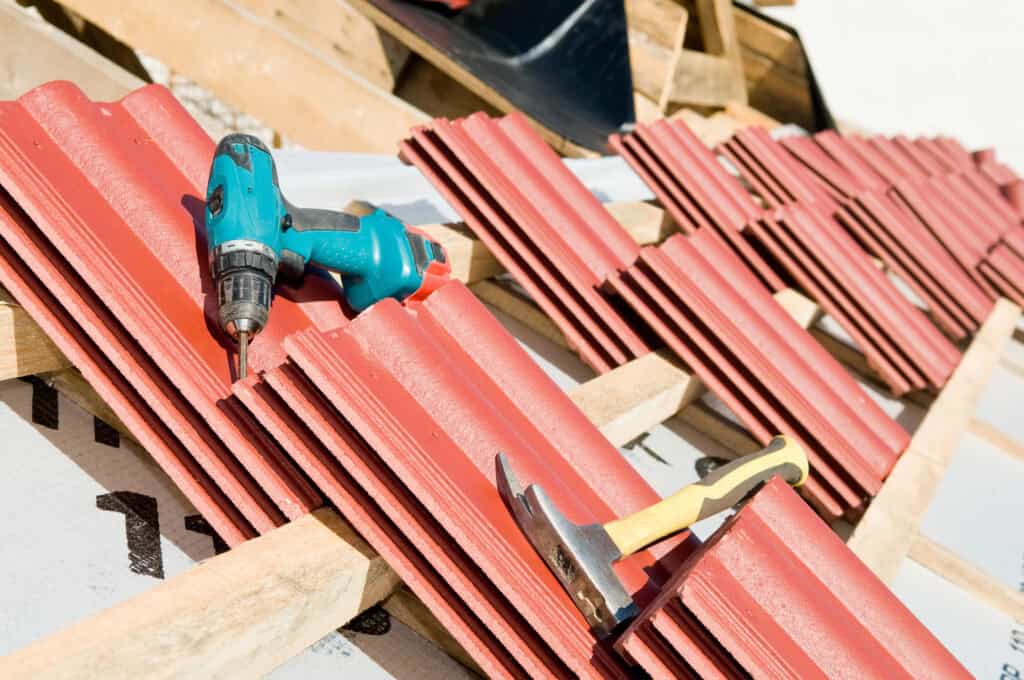Un marteau et une perceuse sans fil reposent sur des tuiles rouges soigneusement disposées sur une structure en bois, indiquant les travaux de construction du toit en cours par un artisan couvreur à Montauban.