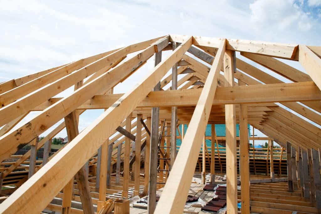 Une charpente en bois en construction contre un ciel partiellement nuageux est vue d'en bas, mettant en valeur le travail artisanal de Charpentier couvreur à Valence d'Agen.