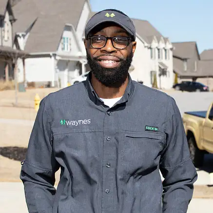 Smiling Waynes Pest Control technician in uniform and cap standing on a suburban street