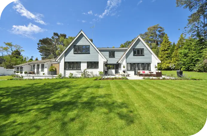 Large modern house with expansive, neatly mowed lawn and patio seating beneath a clear blue sky