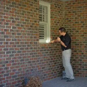 Technician inspecting a window sill on a brick exterior with a flashlight