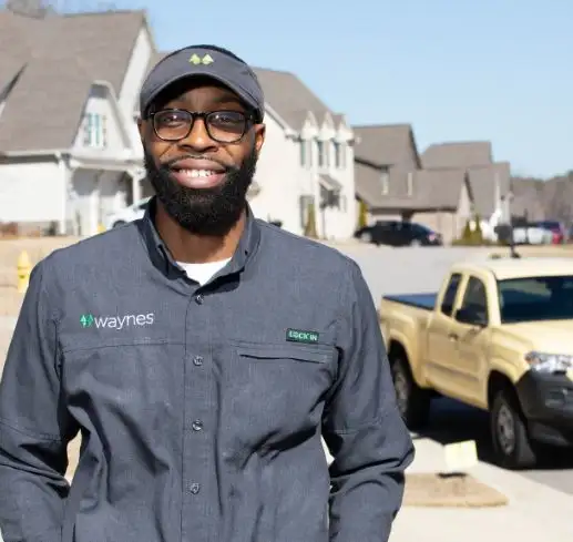Smiling uniformed Waynes technician standing on a suburban street with a company truck parked behind him