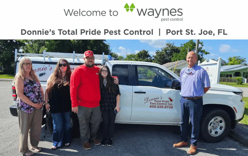 Five people standing beside a white pickup truck with Donnie's Total Pride Pest Control logo