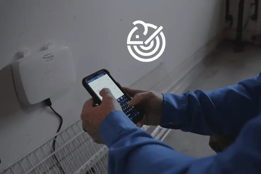 Person holding smartphone to configure a Waynes-labeled SMART pest-control sensor mounted on a wall