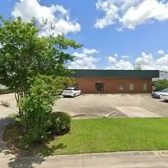 Single-story brick commercial building with parking spaces, a small landscaped tree and a blue sky with clouds