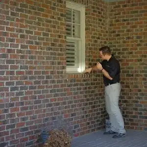 Technician inspecting a window sill on a brick exterior with a flashlight