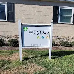 Yard sign reading 'waynes' with green, blue, and yellow diamond icons in front of a beige house