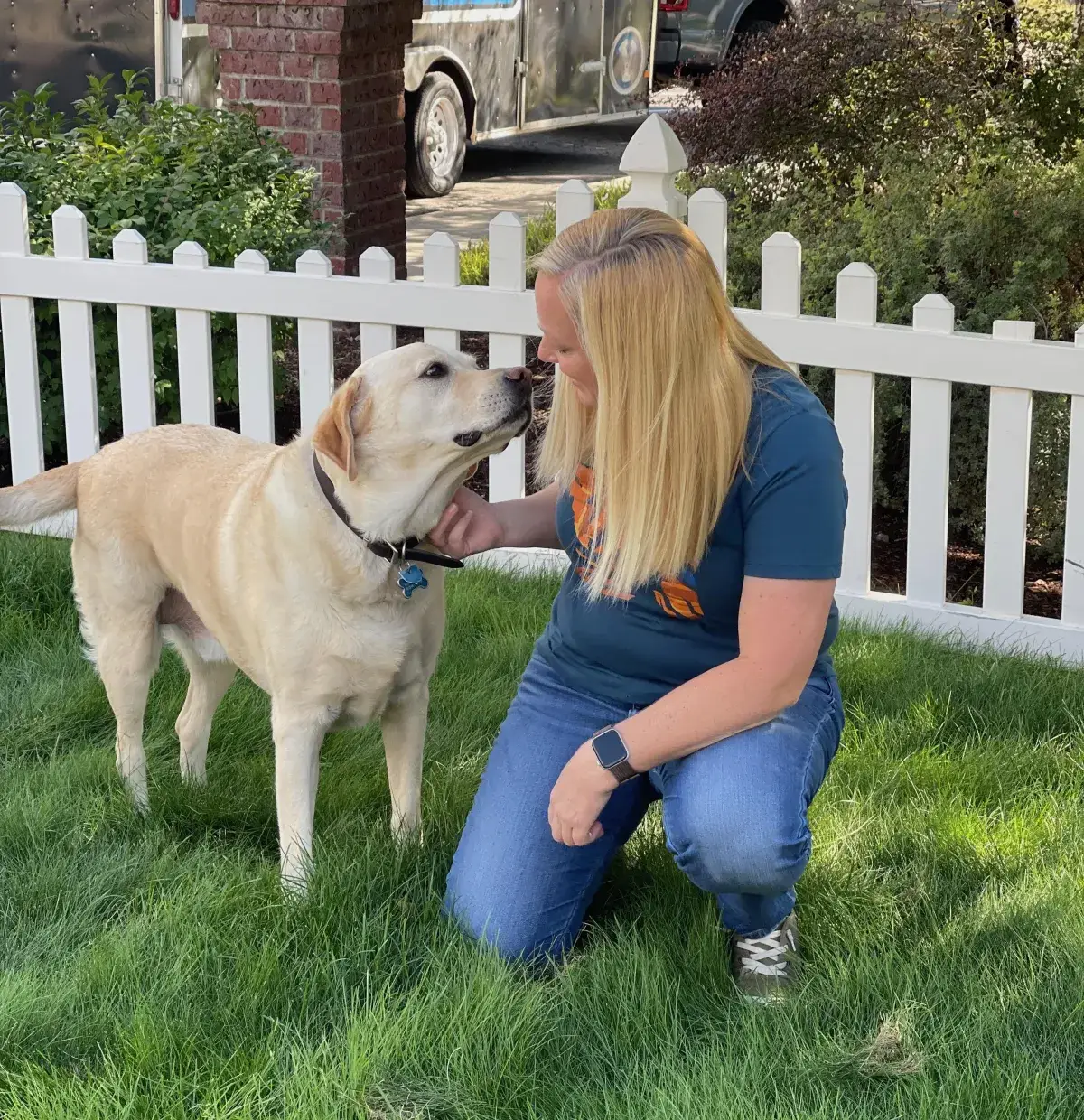 Trainer kneeling with a yellow Labrador in a fenced garden Trainer kneeling with a yellow Labrador in a fenced garden