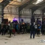 A raw, unadvertised warehouse rave capturing the essence of finding underground electronic music events in 2026. This image represents the 'off-grid' scene where locations are shared via private community networks rather than mainstream platforms