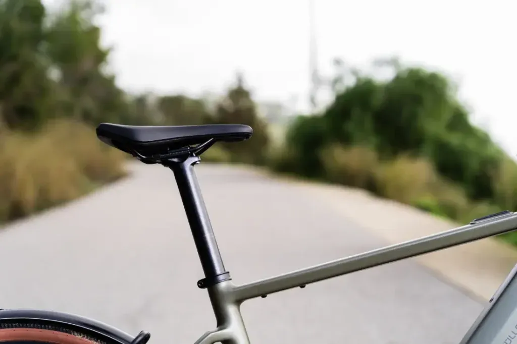 Primer plano de un asiento y un cuadro de bicicleta Riese & Müller en una carretera vacía con vegetación borrosa en el fondo, perfecto para una aventura urbana.