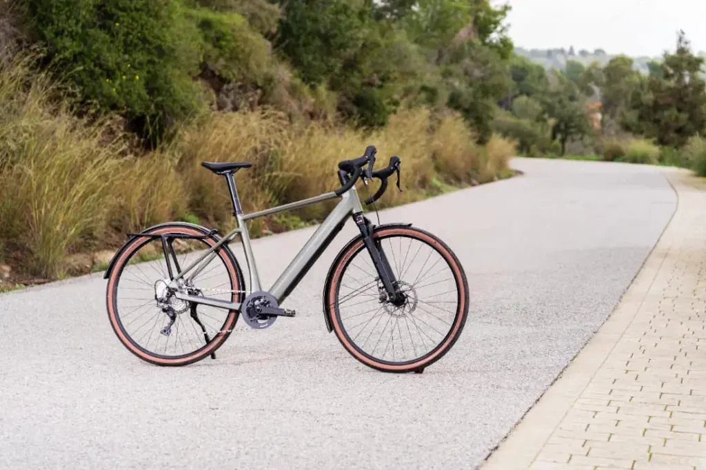 Una elegante bicicleta de ruta, como la versátil UBN Five Commute, se desliza por un camino pintoresco y sinuoso rodeado de exuberante vegetación.