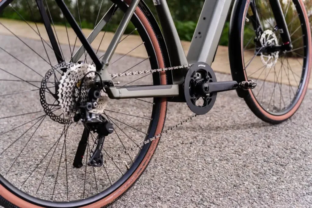 Primer plano de la rueda trasera y el sistema de cambio de una bicicleta Riese & Müller UBN Five en una carretera asfaltada.