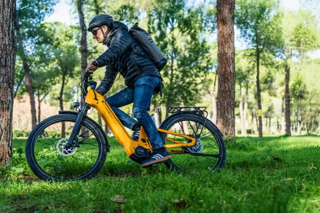 Una persona pasea en una bicicleta eléctrica amarilla Velo de Ville FEB 990 por una zona boscosa, acertando con la opción perfecta para una aventura ecológica.
