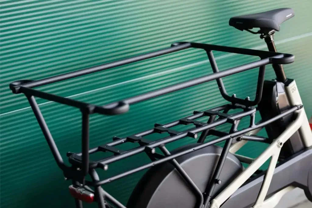 Primer plano del portaequipaje trasero de una bicicleta Moustache Lundi 20 Cargo sobre un fondo verde con rayas horizontales.