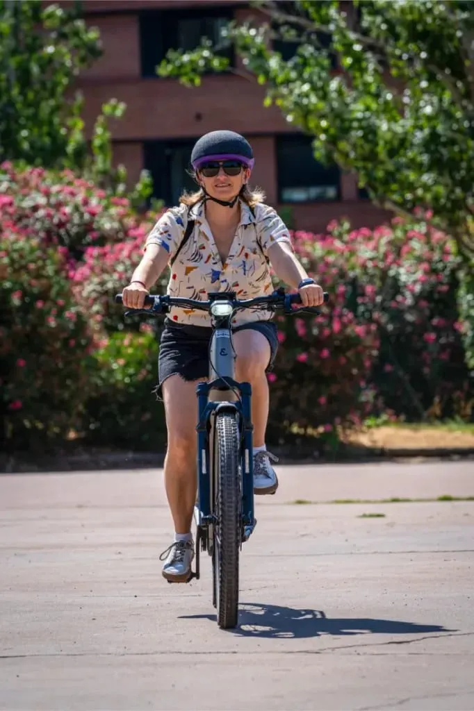 Persona con gorra y gafas de sol monta en una bicicleta Riese & Müller Homage5 al aire libre en un día soleado, con vegetación de fondo.