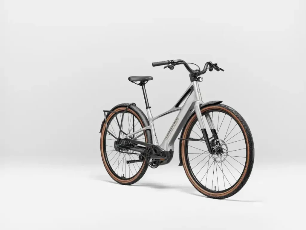 Una bicicleta eléctrica Cannondale FlyingV plateada con neumáticos marrones, asiento y manillar negros sobre un fondo blanco liso.