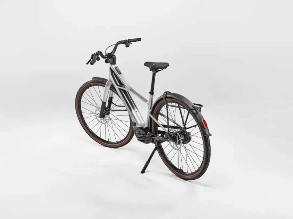 Una bicicleta eléctrica Cannondale FlyingV plateada con guardabarros trasero y pata de cabra, mostrada sobre un fondo blanco liso.