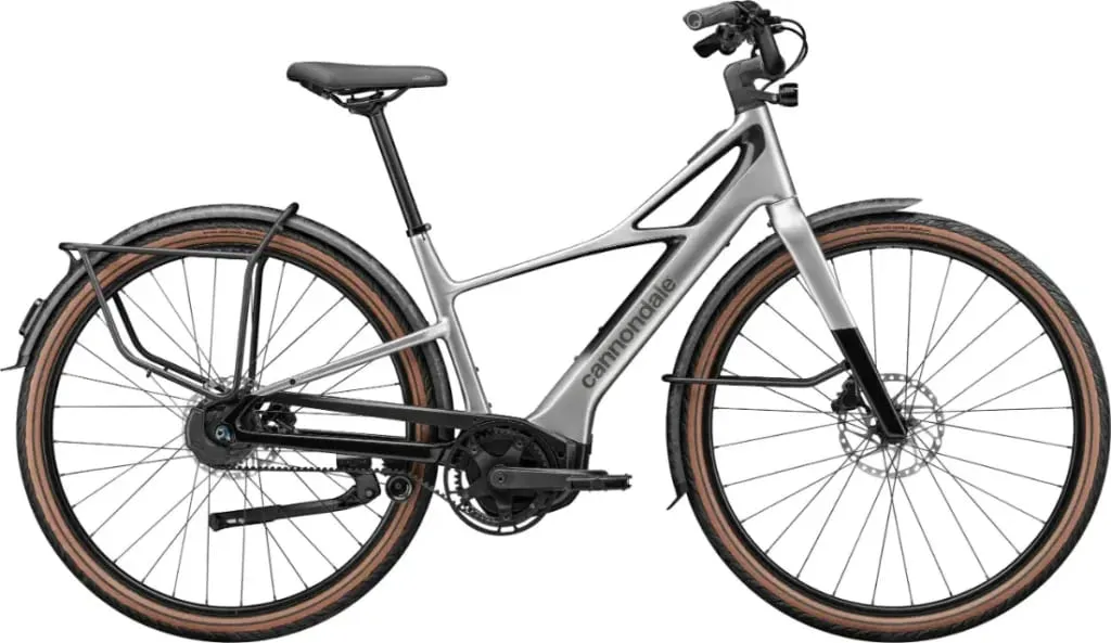 Una bicicleta eléctrica Cannondale FlyingV plateada con guardabarros, portabultos trasero y neumáticos con bordes marrones, mostrada de lado.