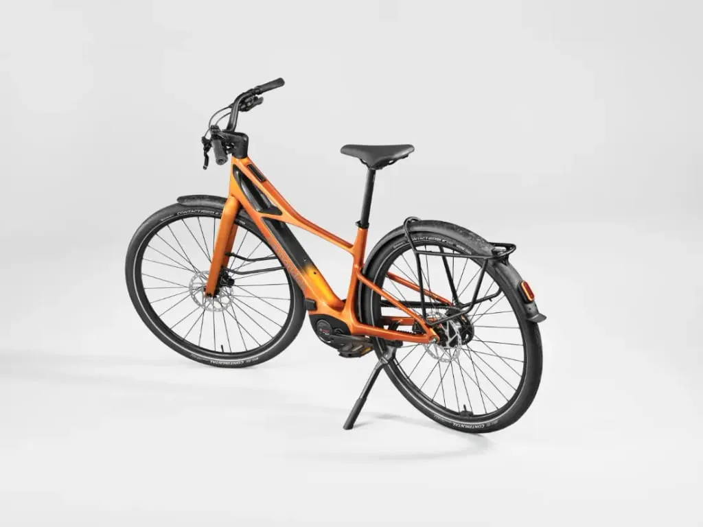 Bicicleta eléctrica Cannondale FlyingV naranja con guardabarros y pata de cabra, fotografiada sobre un fondo blanco liso.