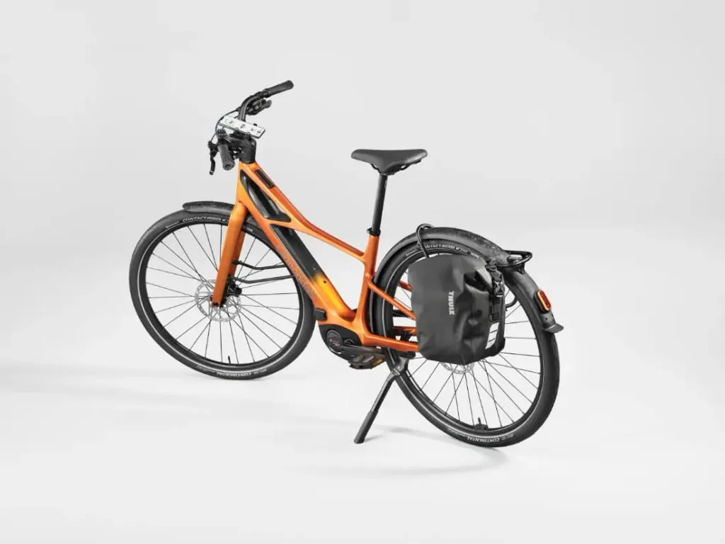Bicicleta eléctrica Cannondale FlyingV de color naranja con bolsa trasera, expuesta en un soporte sobre un fondo blanco liso.