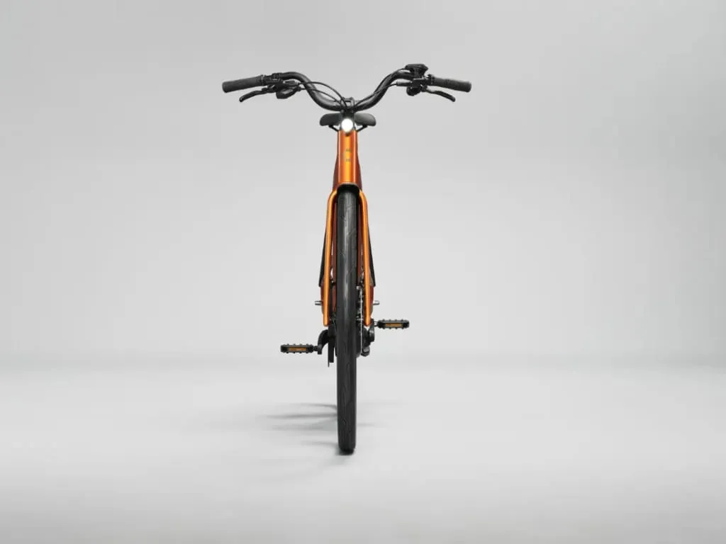 Vista frontal de una bicicleta Cannondale FlyingV naranja con manillar y neumáticos negros, sobre un fondo liso gris claro.