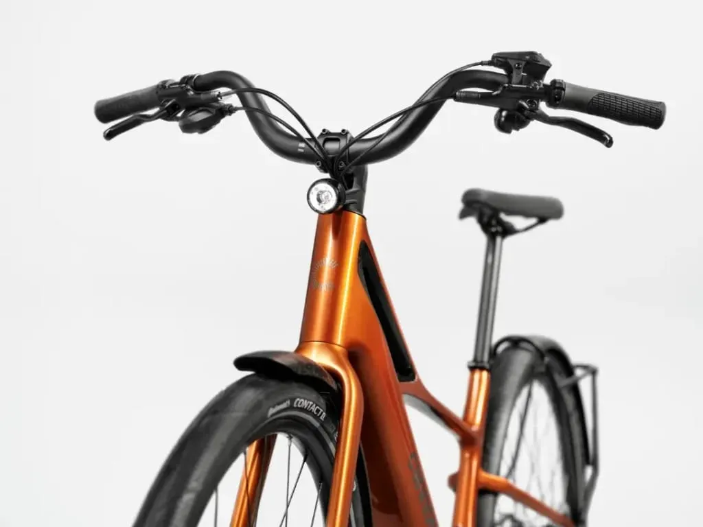 Primer plano de una bicicleta eléctrica Cannondale FlyingV de color naranja, mostrando el manillar, la luz delantera y parte del cuadro sobre un fondo blanco.