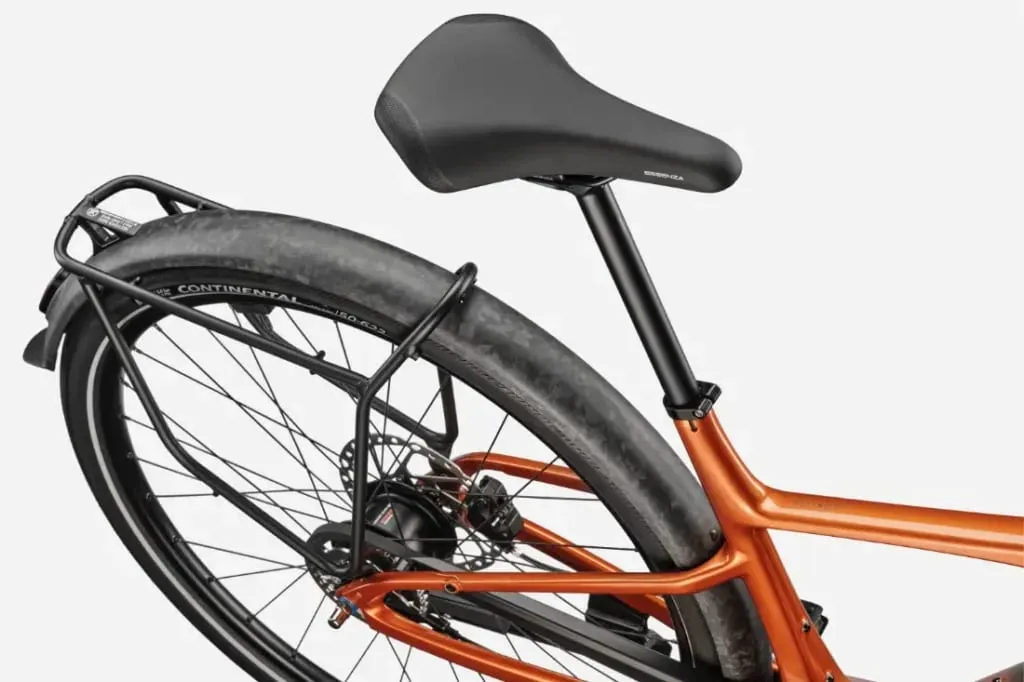 Primer plano de un sillín de bicicleta negro, una rueda trasera y un portabultos metálico sobre un cuadro de bicicleta Cannondale FlyingV naranja.