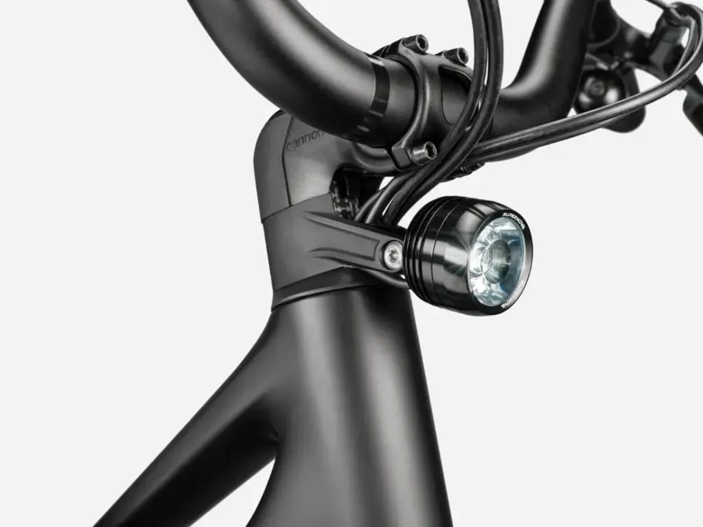 Primer plano de un manillar de bicicleta negro, una potencia y una luz delantera sobre un fondo liso.