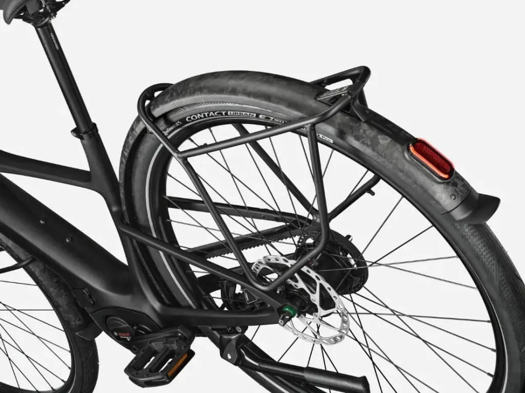 Primer plano de la rueda trasera de una bicicleta, mostrando el neumático, el freno de disco, el portaequipajes y el reflector trasero.