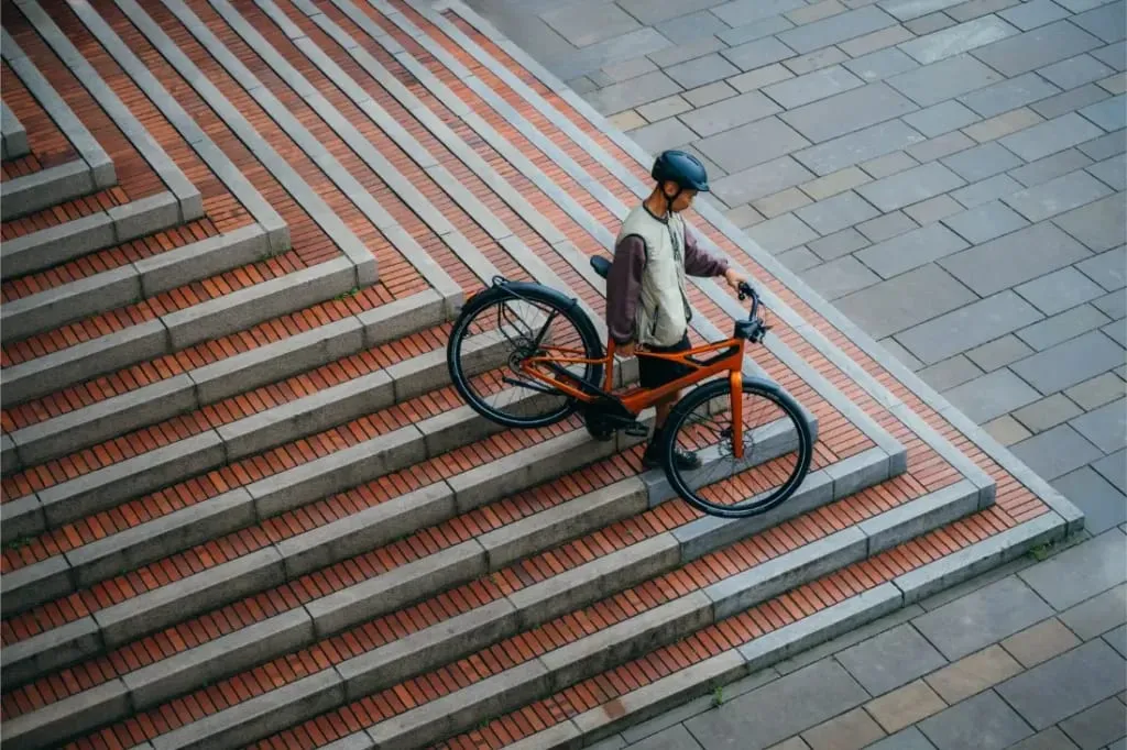 Una persona con casco baja con una bicicleta Cannondale FlyingV por unas anchas escaleras exteriores con un diseño de ladrillos y baldosas.
