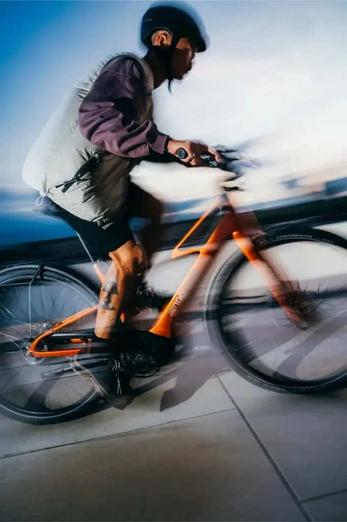 Una persona con casco monta rápidamente en una bicicleta Cannondale FlyingV naranja, creando un efecto de desenfoque de movimiento.