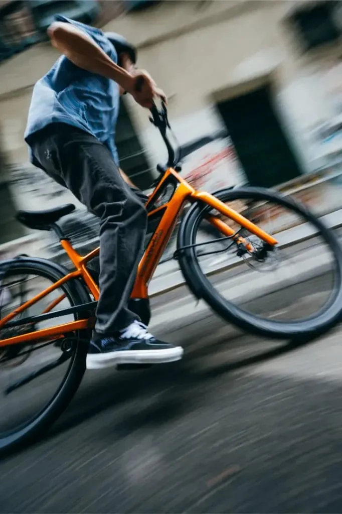 Una persona monta en una bicicleta Cannondale FlyingV naranja a toda velocidad, el desenfoque de movimiento enfatiza el movimiento dinámico a lo largo de una bulliciosa calle de la ciudad.