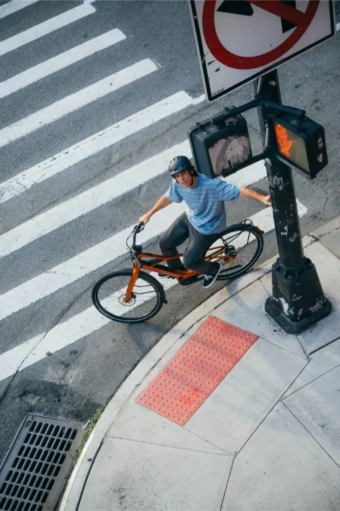 Una persona en una bicicleta Cannondale FlyingV espera en el paso de peatones cerca de una señal de prohibido girar a la izquierda y un semáforo para peatones.