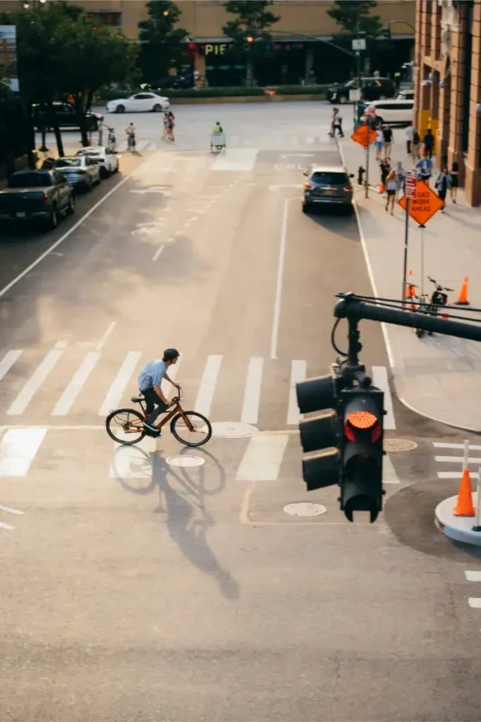 Un ciclista conduce una Cannondale FlyingV por una calle de la ciudad en un paso de peatones cerca de un semáforo y de conos naranjas de obras.