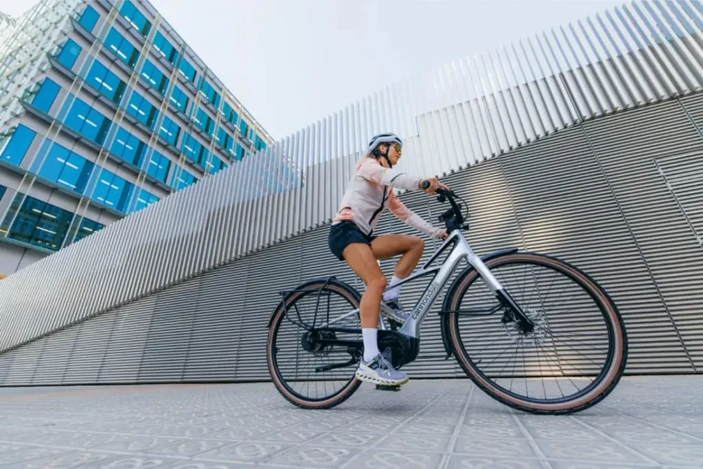 Una persona con casco monta en bicicleta frente a un edificio moderno con una pared metálica estampada.