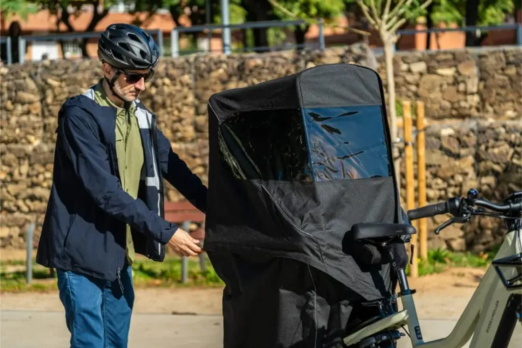 Hombre con casco cerrando la cremallera del compartimento de carga de un remolque Riese & Müller Multicharger3 Mixte Vario al aire libre en un día soleado.