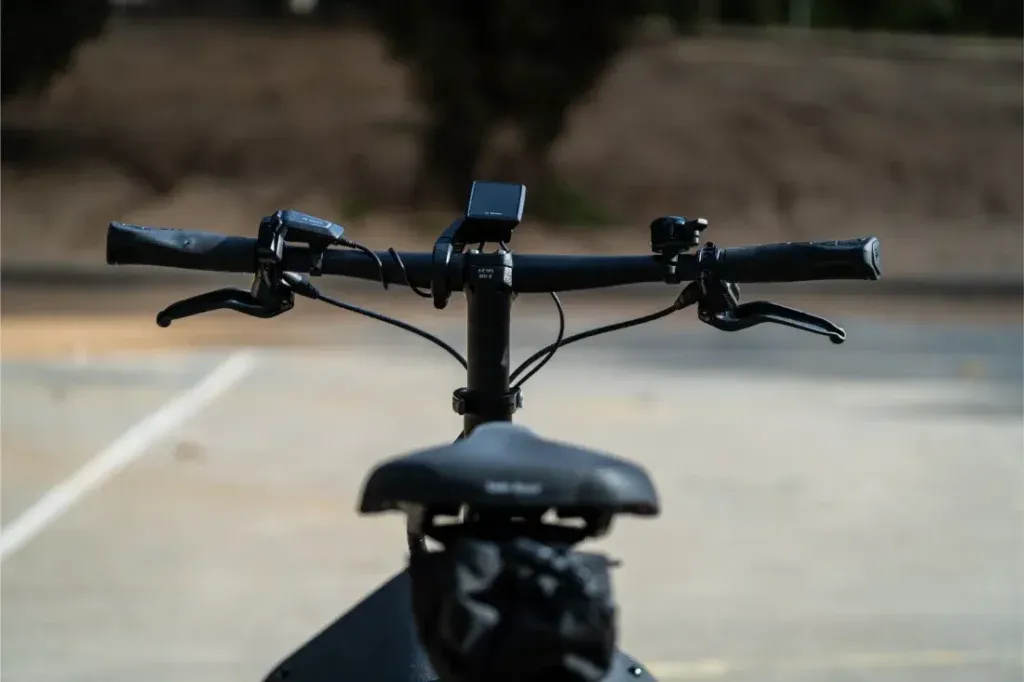 Primer plano del manillar y el sillín de la bicicleta Riese Müller Carrie2, mostrando su tamaño compacto y sus funciones automáticas sobre un fondo borroso al aire libre.