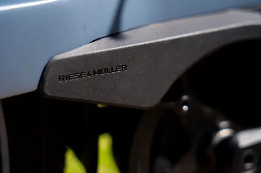 Primer plano de un cuadro negro de bicicleta Riese & Müller Nevo5 con el logotipo "Riese & Müller", parte de la rueda visible a la derecha, que muestra la silenciosa tecnología CORE y un toque de lujo en su elegante diseño.