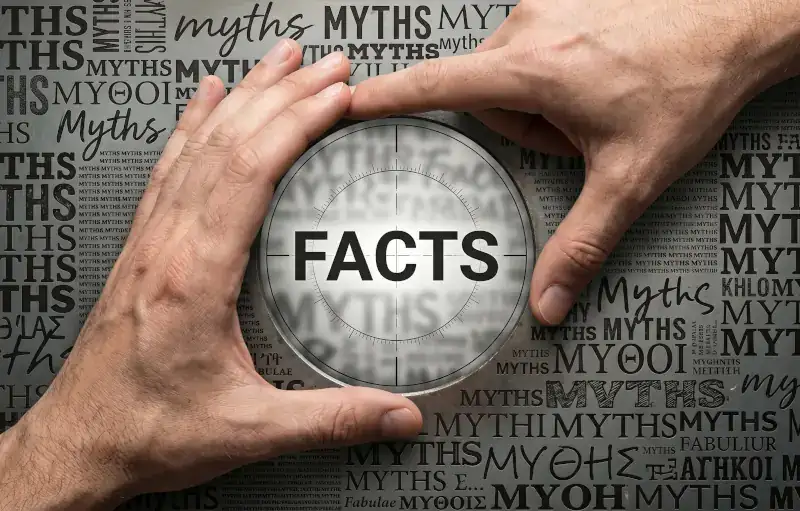 Hands emphasize "FACTS" among faded "MYTHS" on a dark chalkboard.