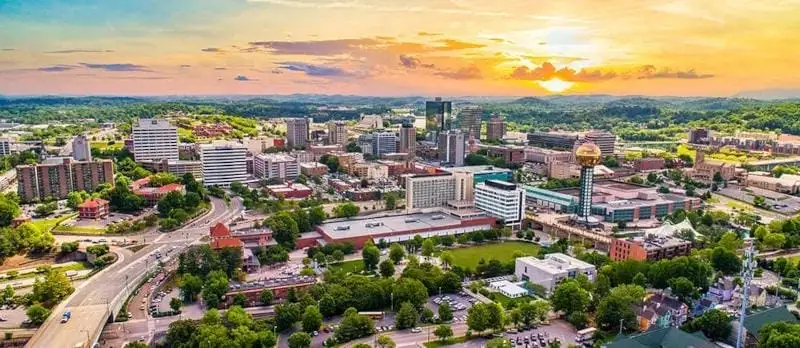 Aerial view of downtown Knoxville, Tennessee at sunset, featuring the Sunsphere and surrounding city buildings with the Smoky Mountains in the distance.