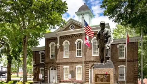 Historic brick courthouse in Loudon, Tennessee, with a soldier statue and American flag in front, surrounded by large trees.