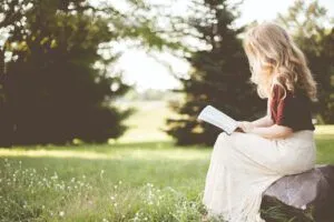 Young woman sitting on a rock reading a Bible in a sunlit meadow, contemplative scene illustrating Why the Number 40 is So Significant in the Bible: Exploring its Meaning and Significance.