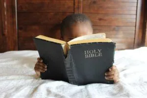 Child reading a worn Holy Bible on a bed, Why the Heart Hardens: Biblical Insights.