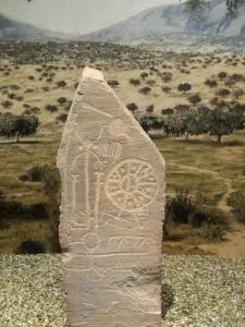 Estela de piedra tallada con petroglifos y un motivo circular tipo rueda en exposición museográfica, La historia detrás de 'cuando vinieron ellos tenían la biblia y nosotros teníamos la tierra'.