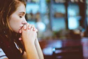 Young woman praying with eyes closed and hands clasped, evoking Why the Good Bible Suffers: Exploring the Dark Side of Faith.