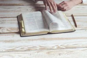 An open annotated Bible on a wooden table with hands turning pages, evoking When the Hebrew Bible was Translated into Greek: A Fascinating Historical Journey.