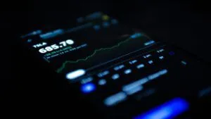Close-up of a smartphone showing TSLA stock price and a rising market chart — What is the Meaning of Yahoo? Find Out Here!